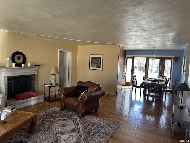 living room featuring a textured ceiling, ornamental molding, a fireplace, and wood finished floors