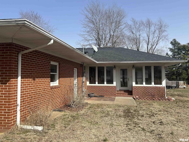 back of house featuring entry steps, a sunroom, roof with shingles, and brick siding