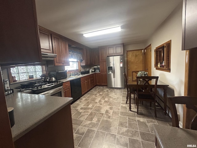 kitchen with stone finish flooring, a sink, under cabinet range hood, and black appliances