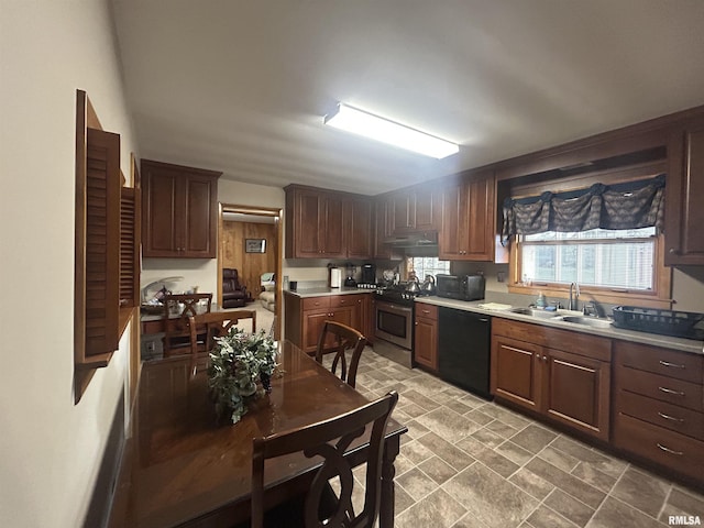 kitchen with stone finish flooring, under cabinet range hood, a sink, light countertops, and black appliances