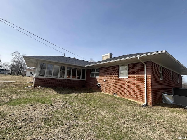 back of property featuring brick siding, a sunroom, a yard, crawl space, and a chimney