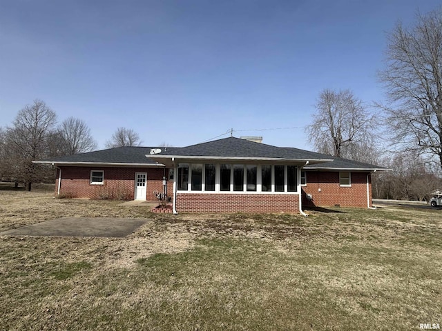 rear view of house with a lawn, a sunroom, roof with shingles, crawl space, and brick siding