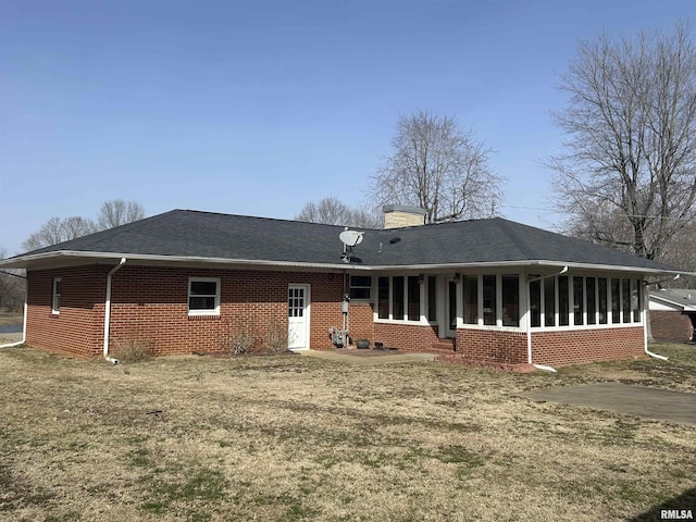 back of house with brick siding, a shingled roof, a sunroom, a lawn, and a chimney