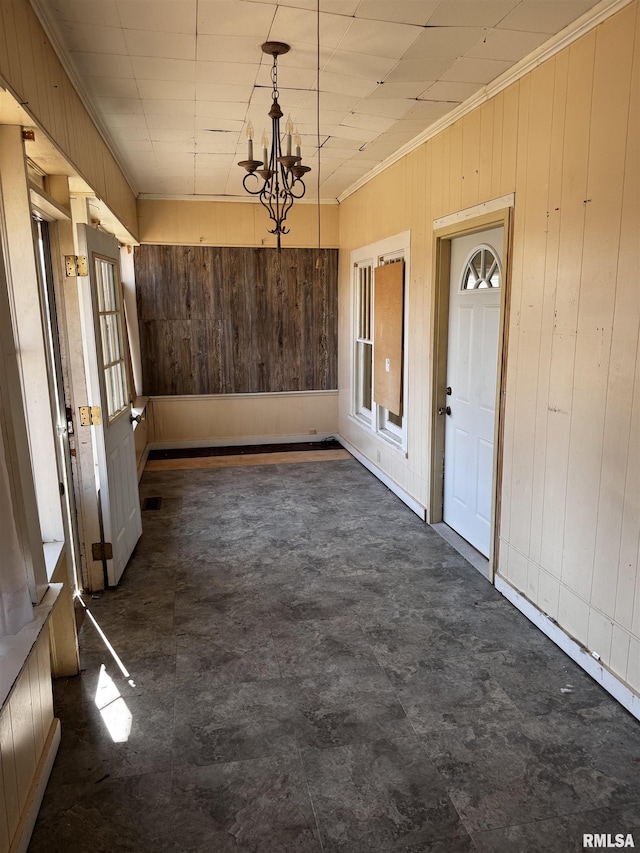 unfurnished dining area featuring wood walls, a chandelier, and crown molding