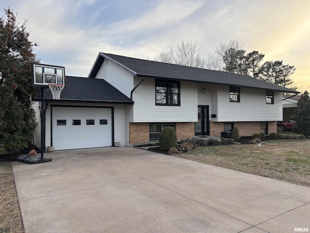 bi-level home with a garage, brick siding, driveway, and a shingled roof