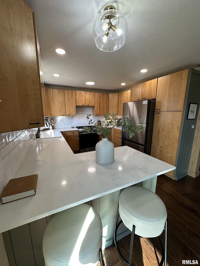 kitchen with brown cabinetry, dark wood finished floors, freestanding refrigerator, a peninsula, and a sink