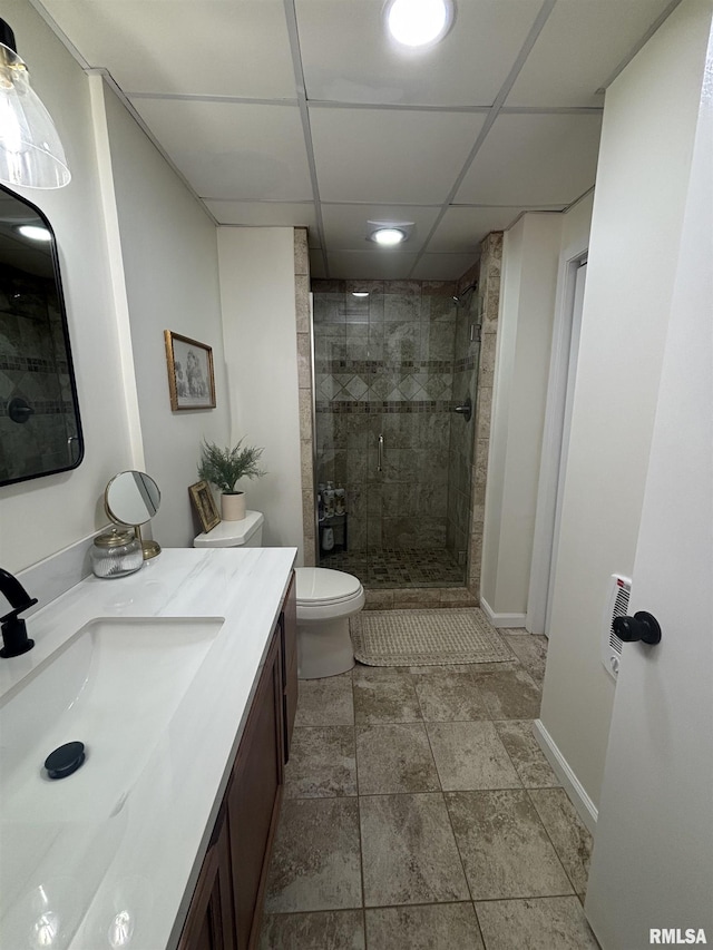 full bath featuring toilet, a stall shower, vanity, a drop ceiling, and baseboards