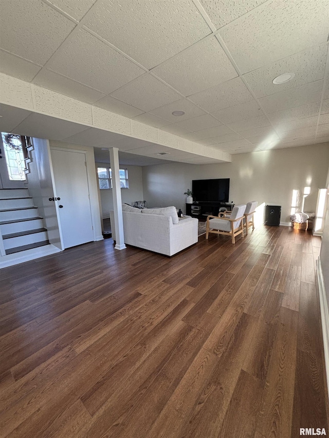 unfurnished living room with a paneled ceiling, dark wood finished floors, stairway, and baseboards