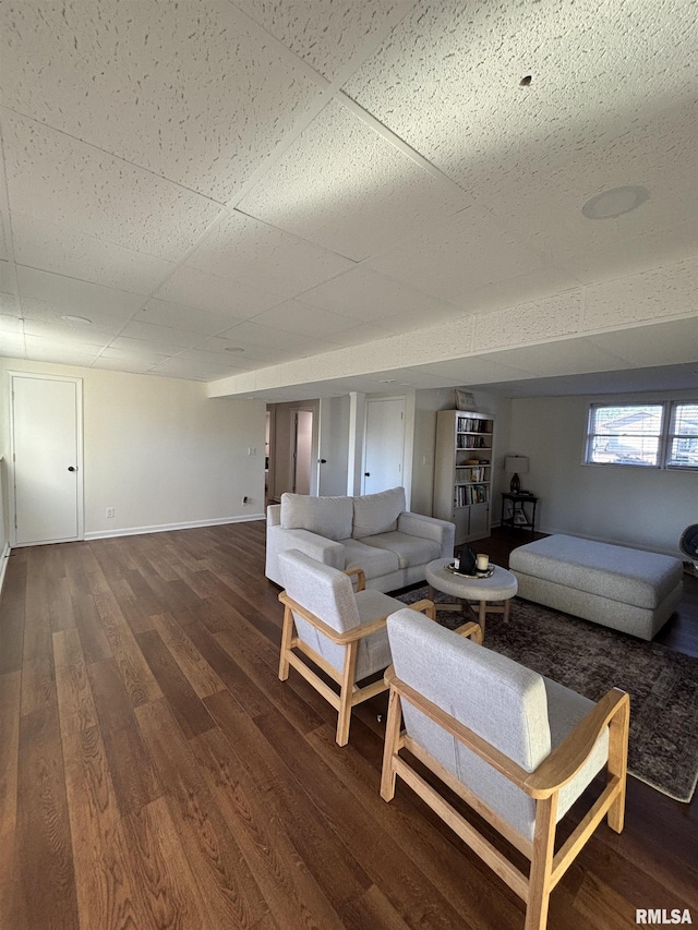 unfurnished living room with a paneled ceiling, baseboards, and wood finished floors