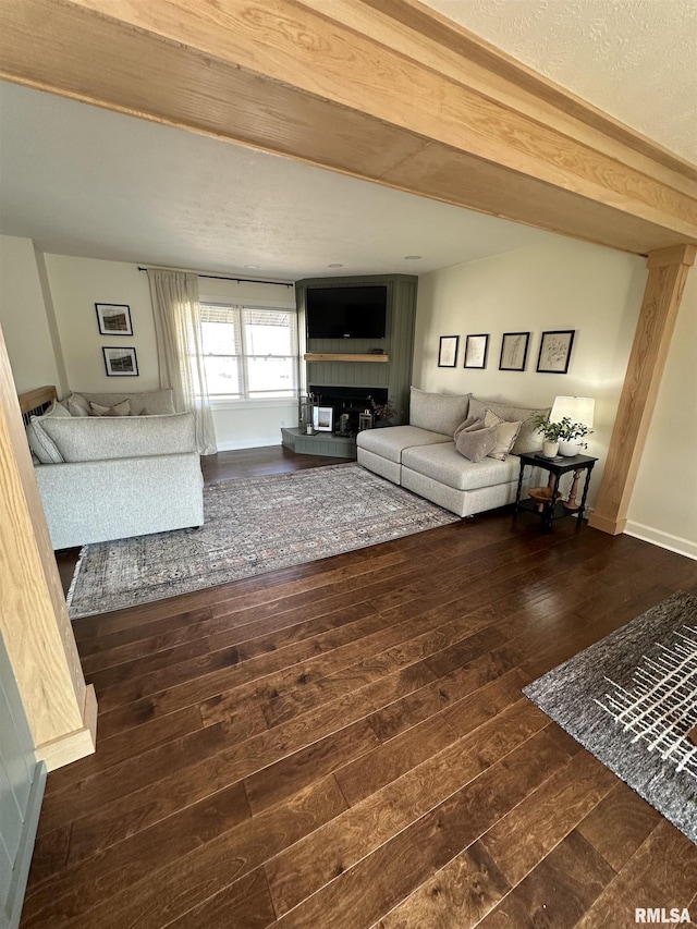 unfurnished living room with hardwood / wood-style flooring, baseboards, a fireplace with raised hearth, and beamed ceiling