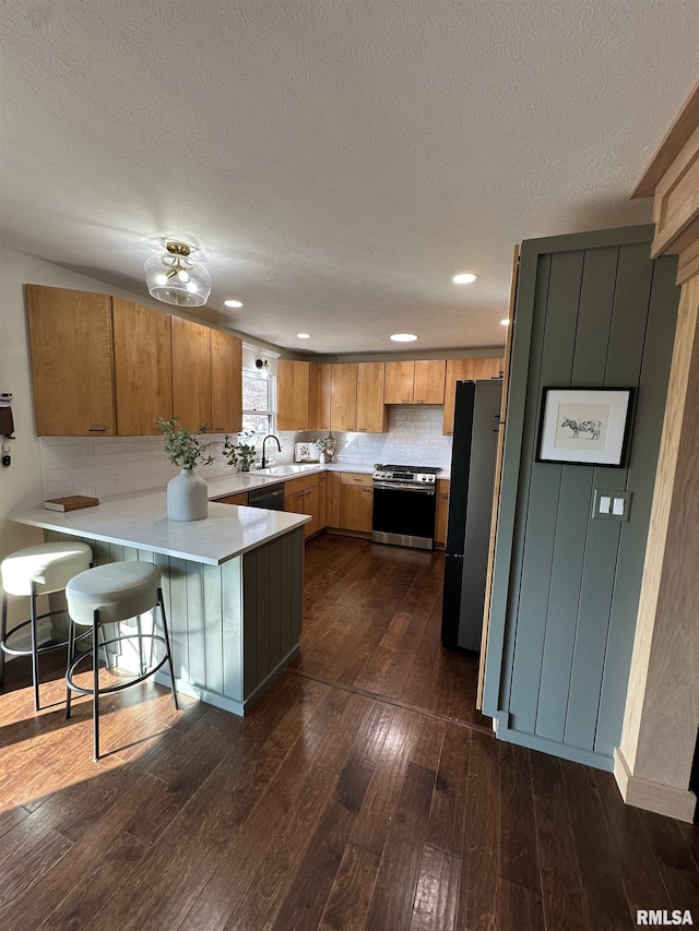 kitchen with a peninsula, light countertops, appliances with stainless steel finishes, brown cabinets, and dark wood-style floors