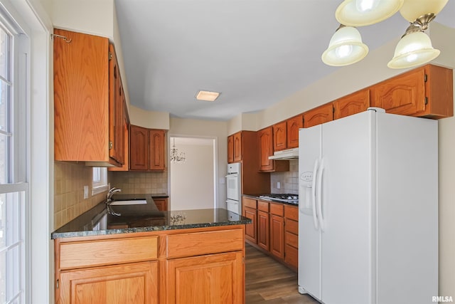 kitchen featuring under cabinet range hood, a peninsula, white appliances, dark wood-style flooring, and a sink