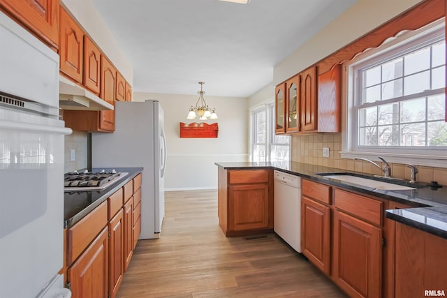 kitchen with white appliances, wood finished floors, a sink, backsplash, and brown cabinets