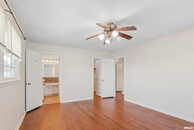 unfurnished bedroom featuring ensuite bath, baseboards, ceiling fan, and wood finished floors