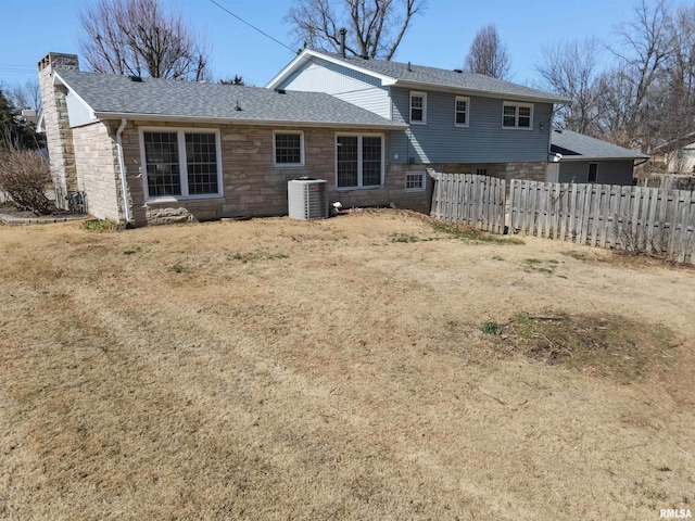 back of property with central air condition unit, stone siding, a chimney, and fence