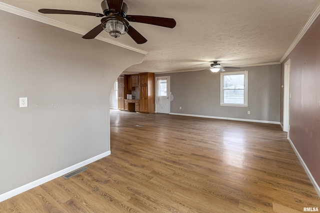 unfurnished room featuring baseboards, arched walkways, crown molding, and wood finished floors