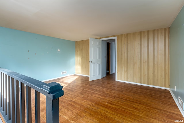 empty room with visible vents, wooden walls, baseboards, and wood finished floors