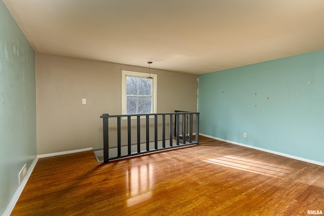 empty room featuring wood-type flooring, visible vents, and baseboards