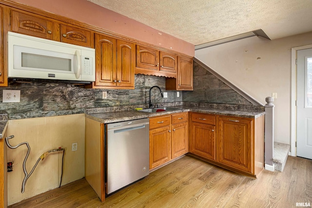 kitchen featuring white microwave, a sink, light wood-style floors, dishwasher, and brown cabinetry