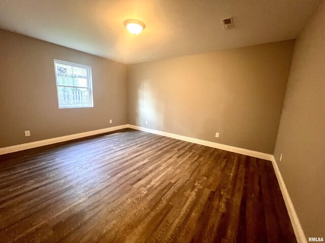 empty room with dark wood-type flooring, baseboards, and visible vents