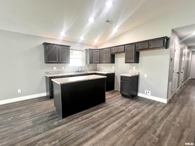 kitchen featuring visible vents, a sink, dark wood-style floors, a center island, and vaulted ceiling