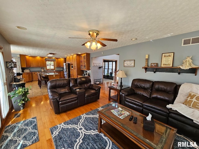 living area featuring ceiling fan, visible vents, light wood finished floors, and a textured ceiling