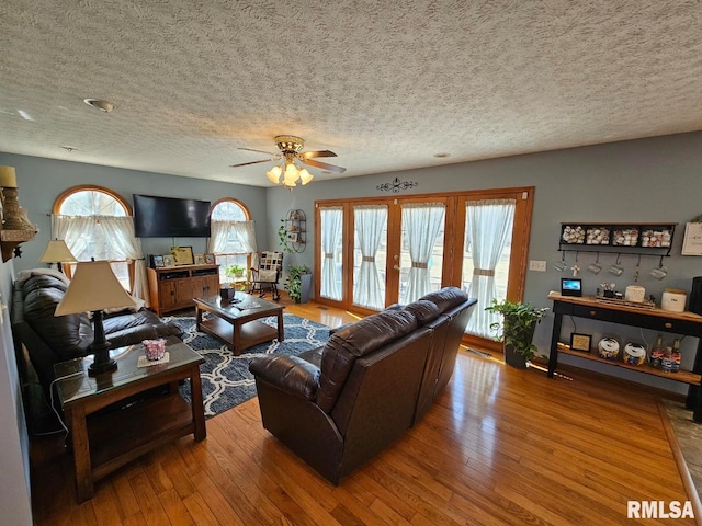 living room featuring wood-type flooring, a textured ceiling, and ceiling fan