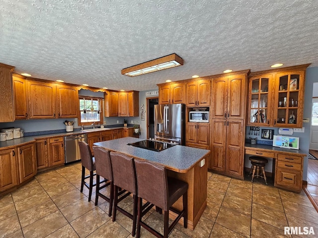 kitchen featuring a breakfast bar, built in desk, appliances with stainless steel finishes, brown cabinetry, and a sink