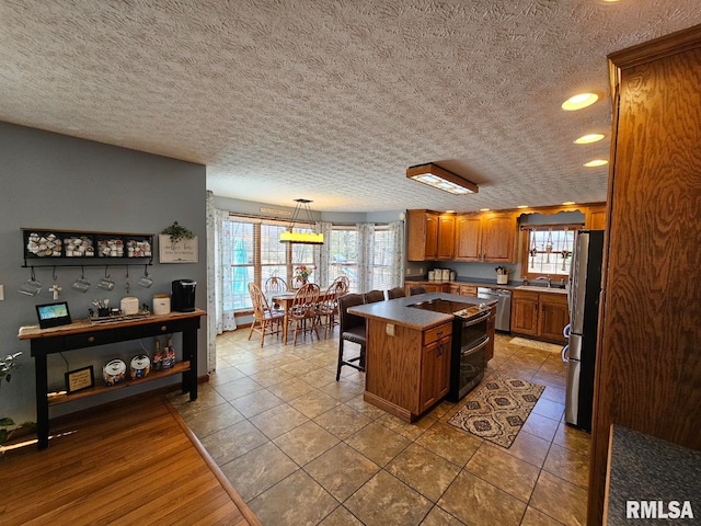 kitchen with brown cabinetry, a kitchen island, freestanding refrigerator, a sink, and stainless steel dishwasher