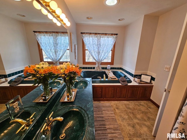 bathroom with tile patterned flooring, a garden tub, and a sink