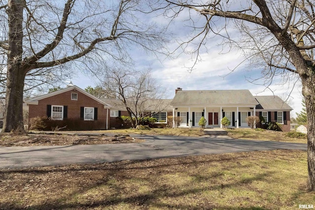 view of front facade with aphalt driveway, covered porch, brick siding, and a chimney