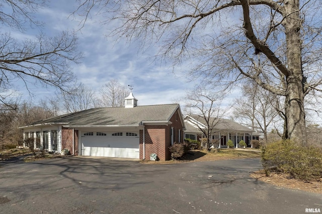 view of side of home with aphalt driveway, an attached garage, brick siding, and a chimney