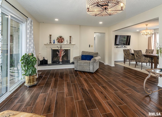 sitting room with a textured ceiling, an inviting chandelier, a fireplace with raised hearth, and wood tiled floor