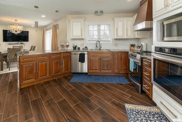 kitchen featuring stainless steel appliances, wall chimney exhaust hood, wood tiled floor, and a sink