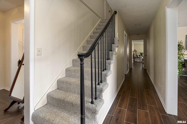 stairway featuring baseboards, a textured ceiling, and wood finish floors