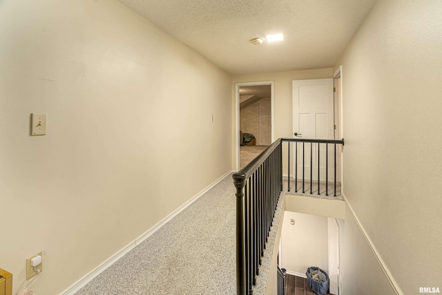 hall with an upstairs landing, carpet flooring, a textured ceiling, and baseboards