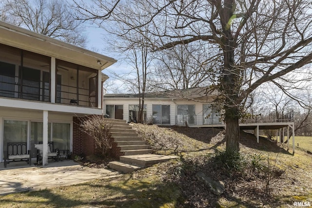 view of side of home featuring stairway, a patio area, brick siding, and a sunroom