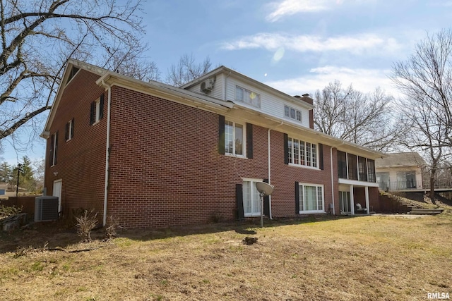 rear view of property featuring brick siding, central AC unit, a chimney, and a yard