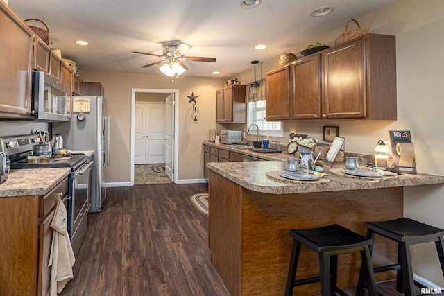 kitchen featuring brown cabinets, dark wood finished floors, stainless steel appliances, a peninsula, and baseboards