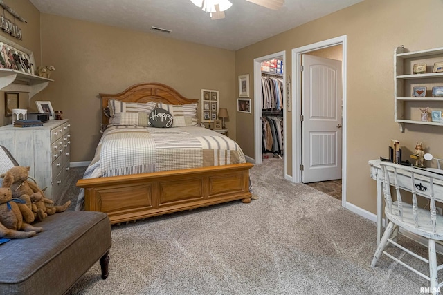 carpeted bedroom with visible vents, a walk in closet, a closet, baseboards, and ceiling fan