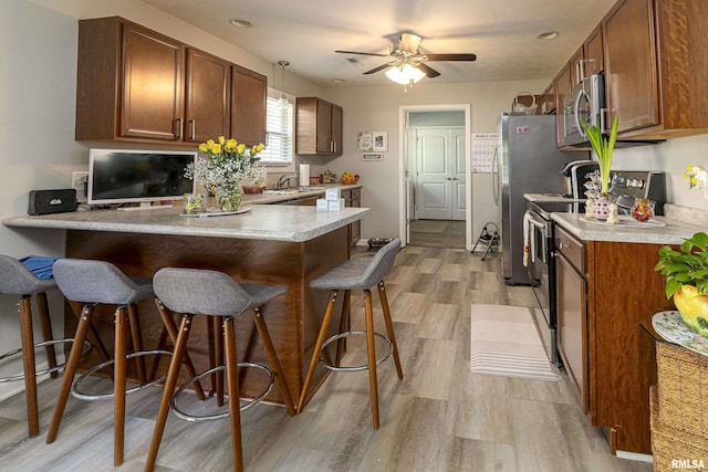 kitchen featuring a breakfast bar, light countertops, appliances with stainless steel finishes, a peninsula, and a sink