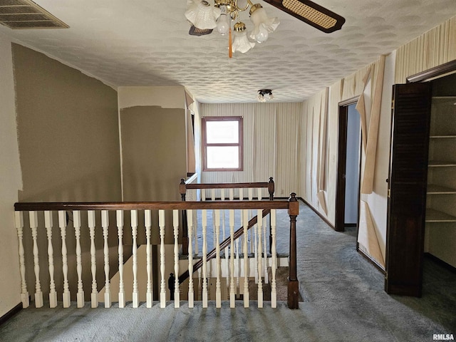 corridor featuring an upstairs landing, visible vents, carpet floors, and a textured ceiling