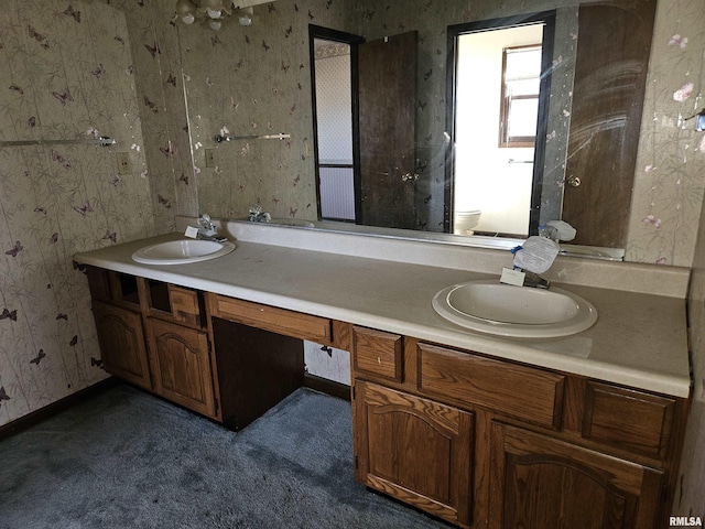 bathroom featuring double vanity, toilet, wallpapered walls, and a sink