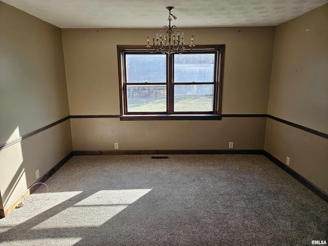 carpeted spare room featuring visible vents, an inviting chandelier, and baseboards