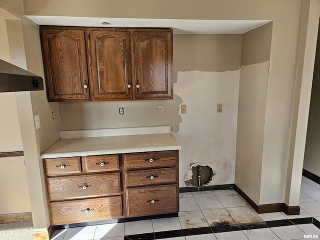 kitchen featuring light countertops, wall chimney exhaust hood, light tile patterned flooring, and baseboards