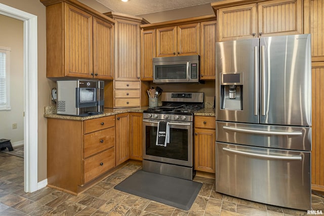 kitchen featuring stainless steel appliances, light stone countertops, baseboards, and brown cabinetry