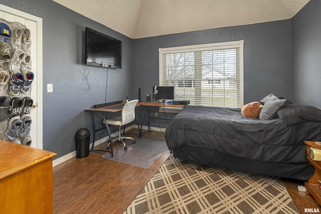 bedroom with lofted ceiling, wood finished floors, baseboards, and a textured wall