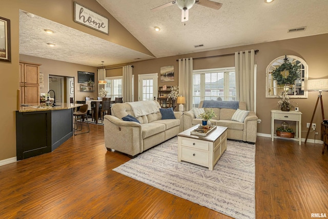 living room featuring visible vents, baseboards, lofted ceiling, wood finished floors, and a textured ceiling