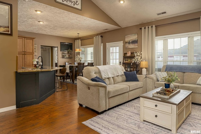 living area featuring visible vents, baseboards, vaulted ceiling, wood finished floors, and a textured ceiling