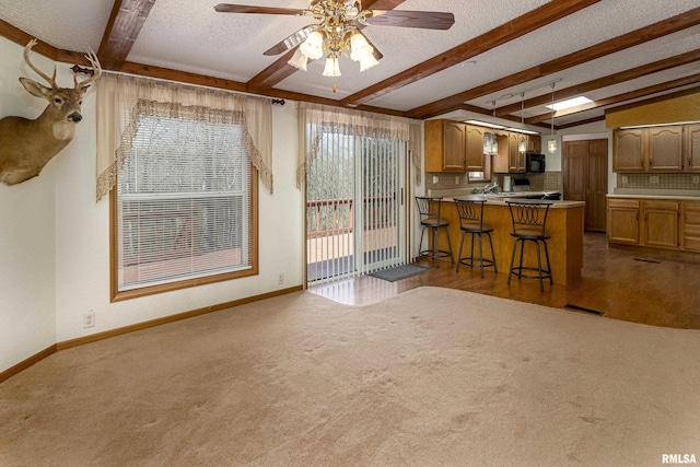 kitchen with a wealth of natural light, dark carpet, a textured ceiling, and lofted ceiling with beams